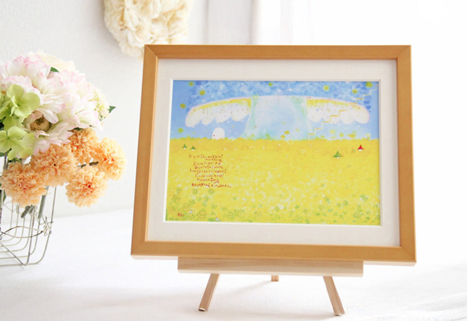 黄色い野原と青い空を描いた作品をイーゼルに飾った写真