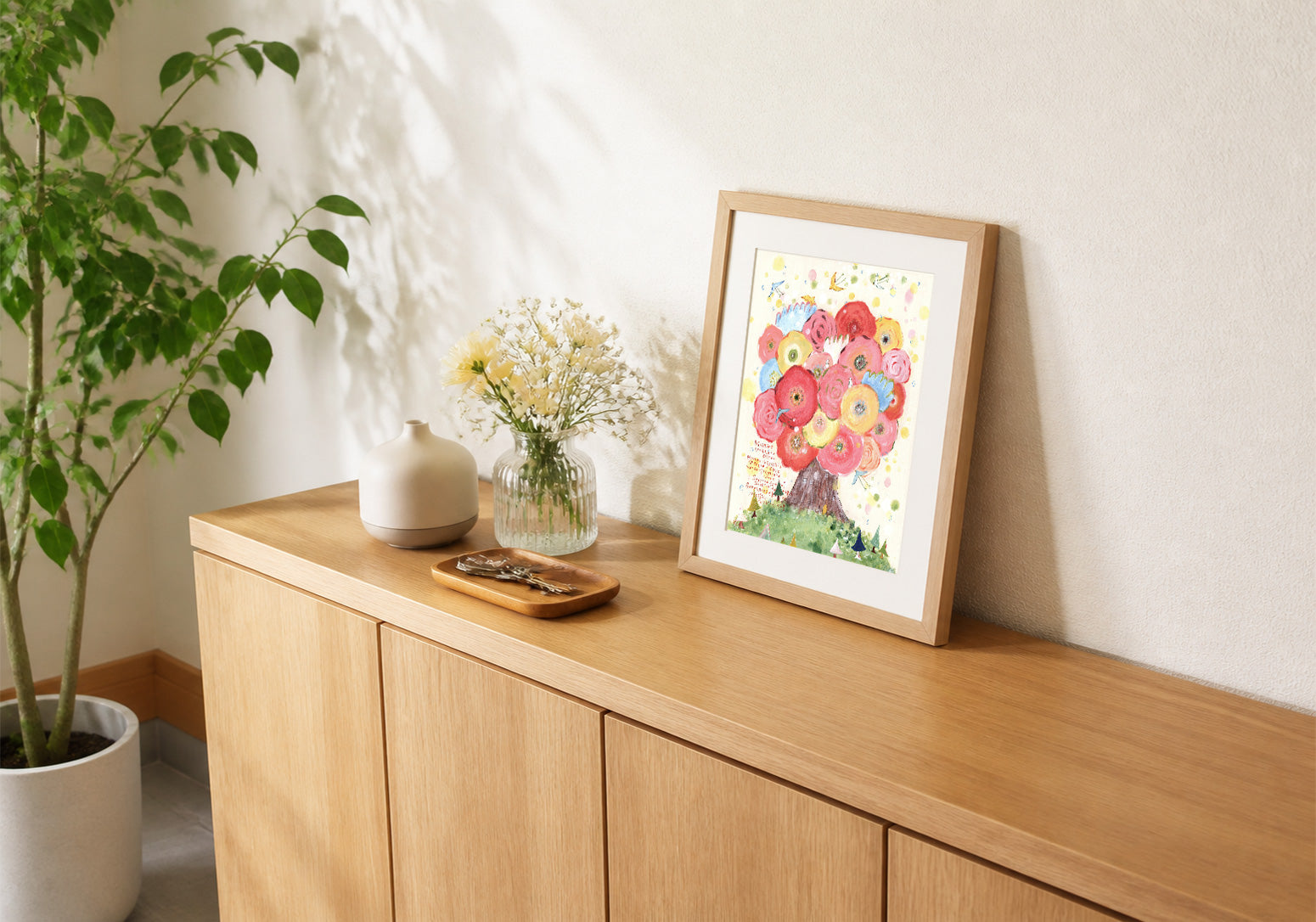 玄関収納の上に花を描いた作品をオークの額で飾った例