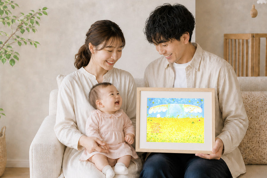 ソファで赤ちゃんを抱いたご両親が、菜の花畑を描いた額装作品を手に笑顔を見せる様子