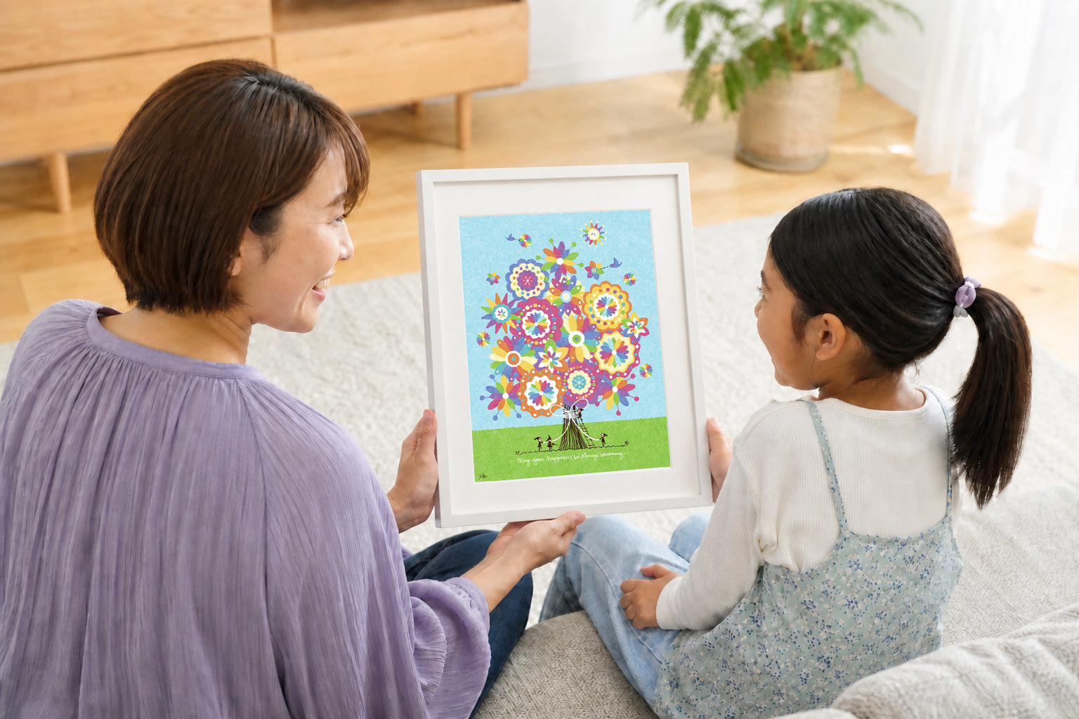 母親と女の子が、家族のつながりを描いた額装された絵を一緒に眺める様子