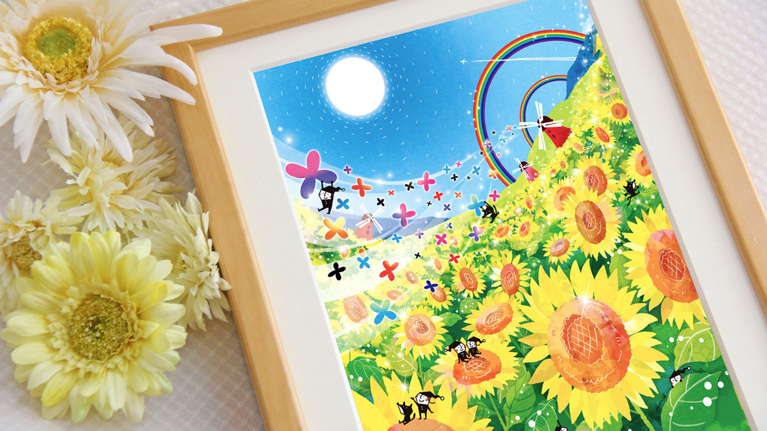 ひまわりと虹、光あふれる空を描いたKAWAII ARTの額装された絵を花とともに写した拡大写真