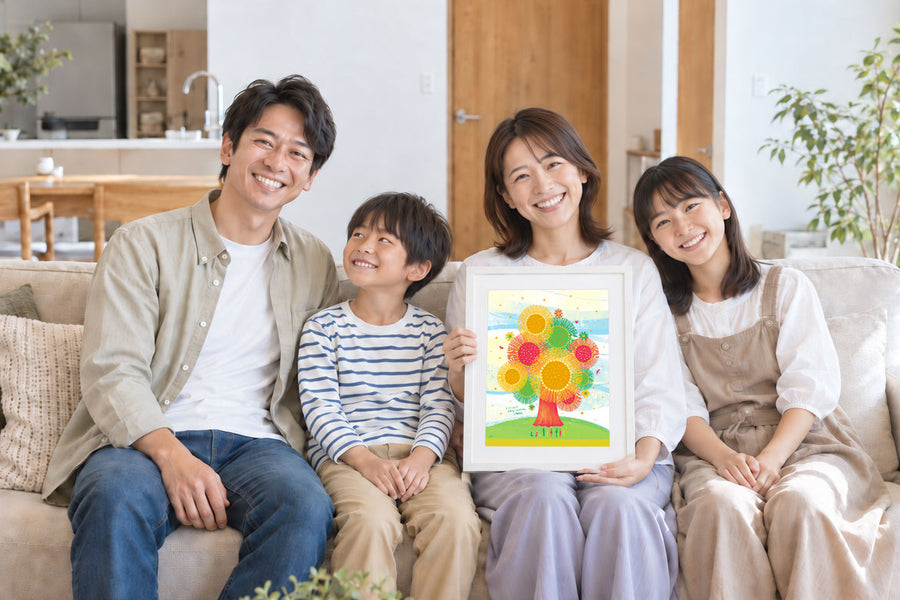 新しい住まいのリビングで、家族4人が額に入れた絵を囲んで笑顔を見せる様子