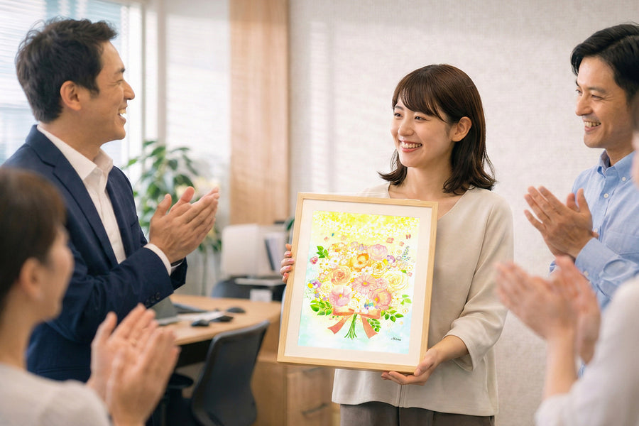 職場で同僚に拍手で送られながら、花束の絵「光」を受け取って笑顔を見せる女性