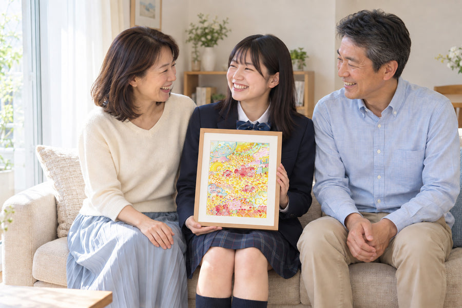 制服姿の高校生が、両親にはさまれてソファに座り、花畑の絵「陽だまり」を手に笑顔を見せる様子