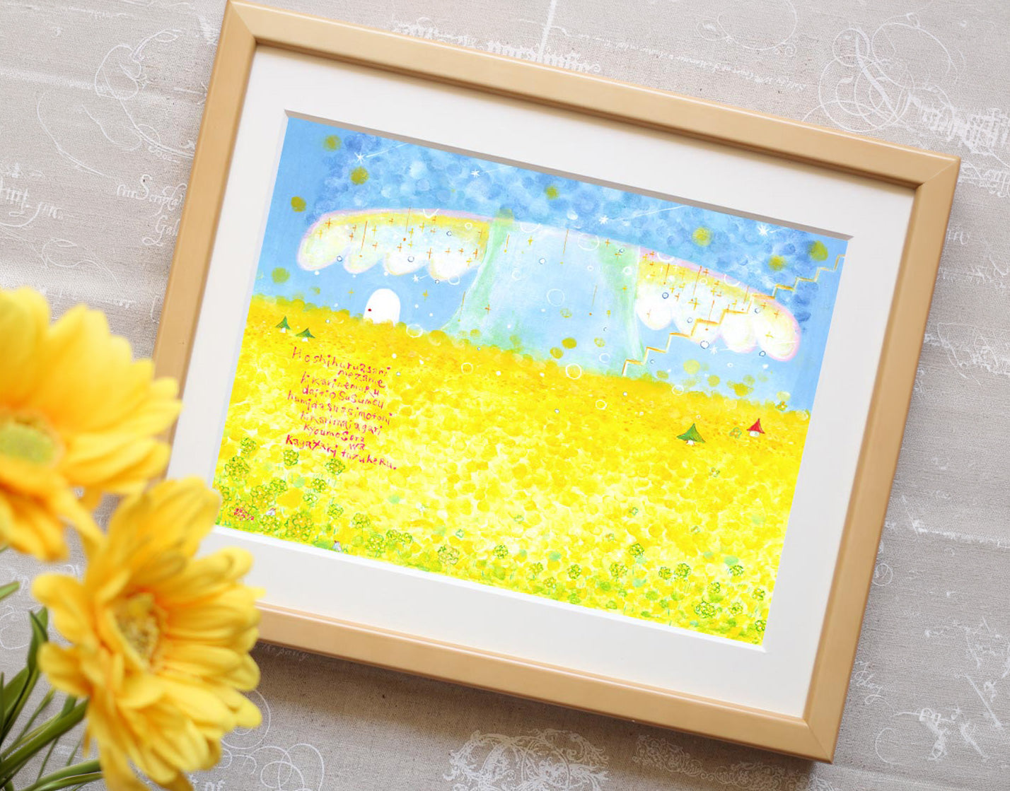 菜の花畑の絵「Kibou ‐ 希望 ‐」と黄色い花を飾った写真